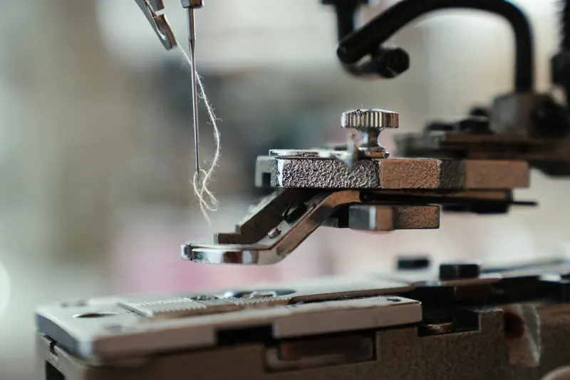 Detailed view of a sewing machine needle threading fine thread, showcasing precision in tailoring and craftsmanship