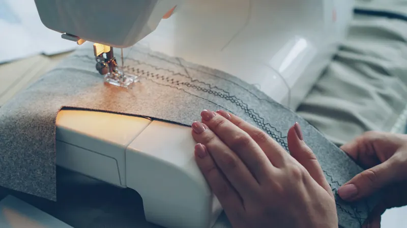 Hands guiding fabric through a sewing machine, stitching pattern