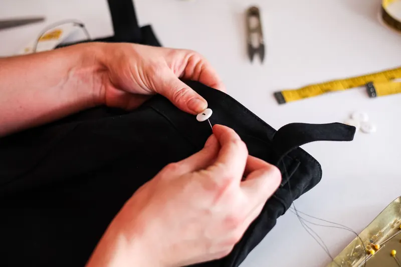 Close-up of hands skillfully sewing a button on black fabric, showcasing attention to detail