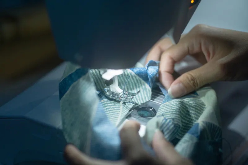 Hands guiding fabric through a sewing machine, showcasing precision and craftsmanship