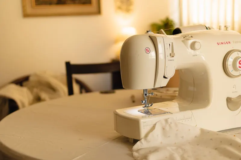 White sewing machine on a table in a cozy indoor setting, with soft lighting